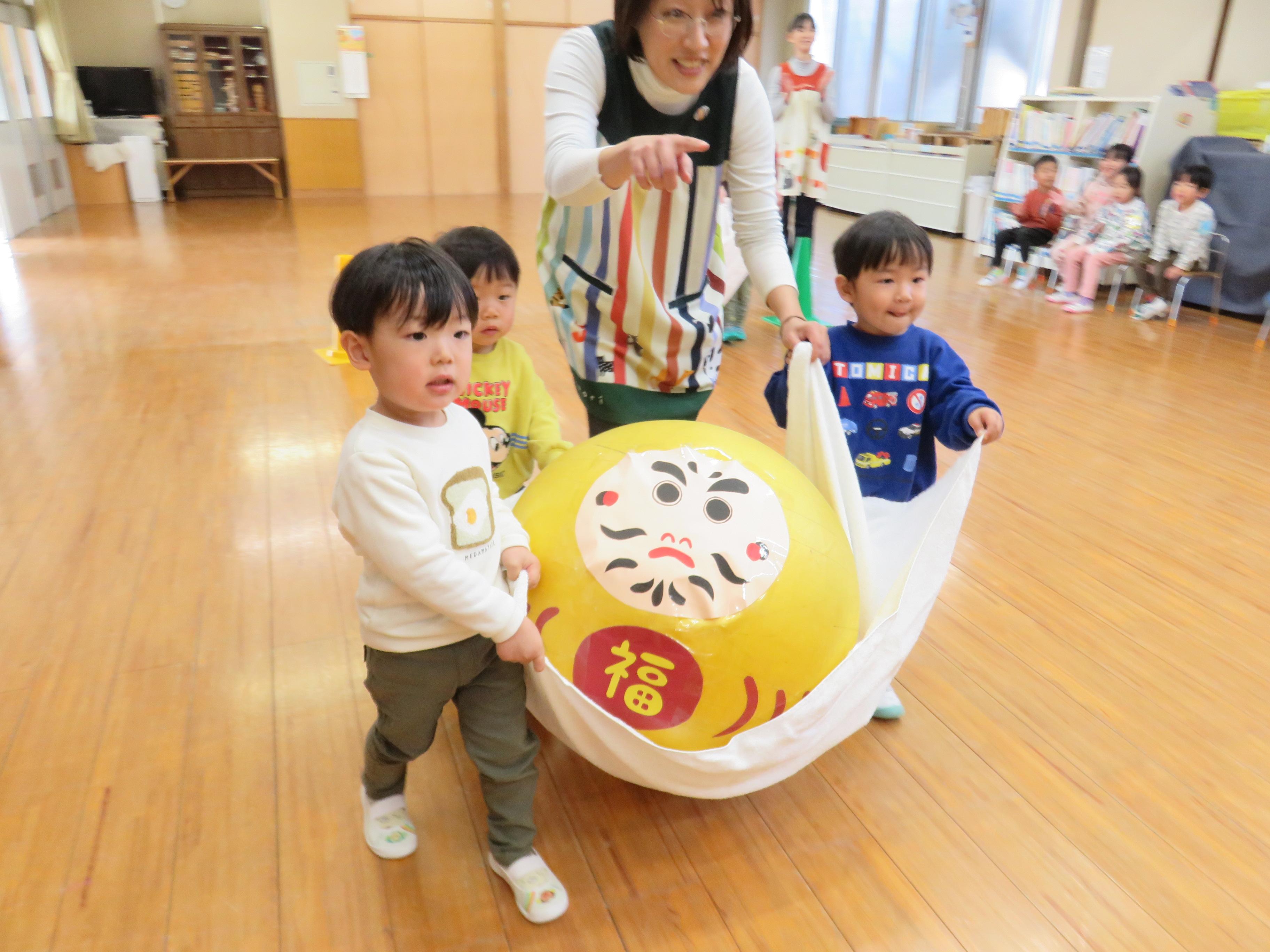 保育士と子ども達で協力してだるま運びを楽しんでいる写真