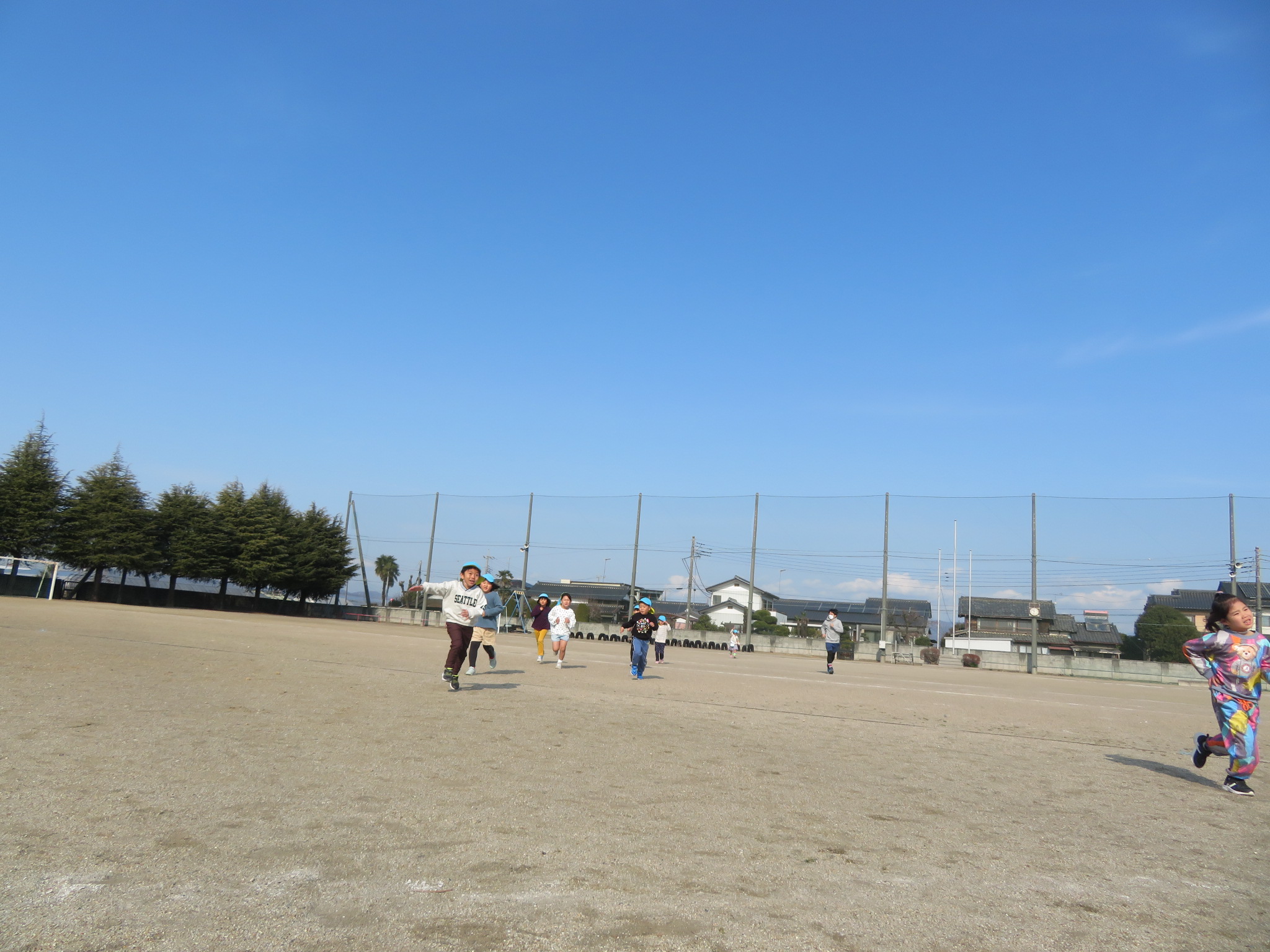 広い小学校の校庭を元気に走り回る子ども達の写真